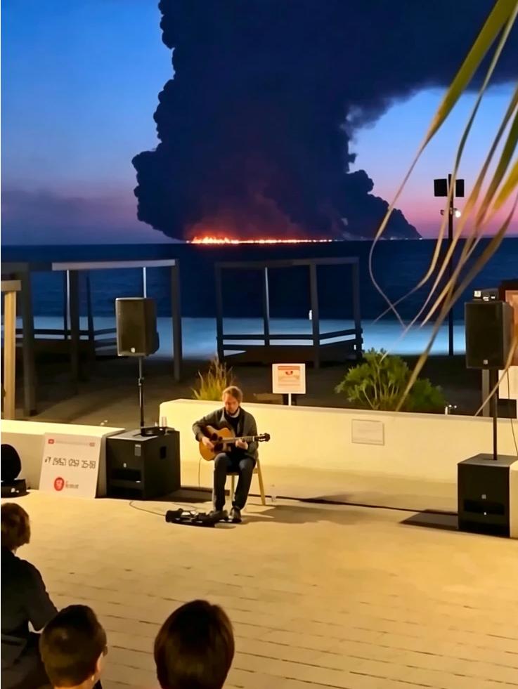 滚滚浓烟下，一名俄罗斯男子在海边淡定的弹奏吉他！