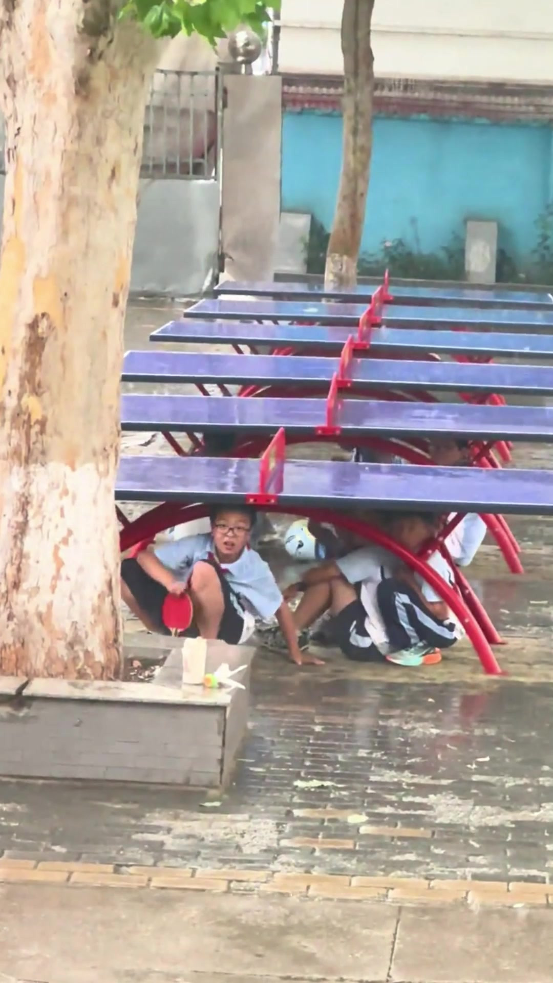 突逢降雨，孩子们钻到乒乓球桌下方躲雨，乒乓球桌躲雨谁的童年？
